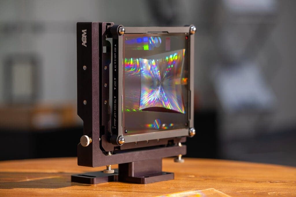 An AOM computer-generated hologram (CGH) used for measuring an off-axis parabolic optic reflects rainbows of light while mounted on an AOM stage.
