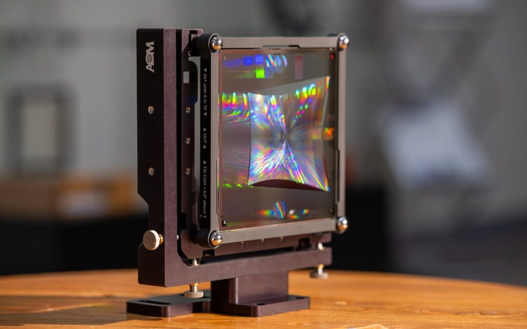 An AOM computer-generated hologram (CGH) used for measuring an off-axis parabolic optic reflects rainbows of light while mounted on an AOM stage.